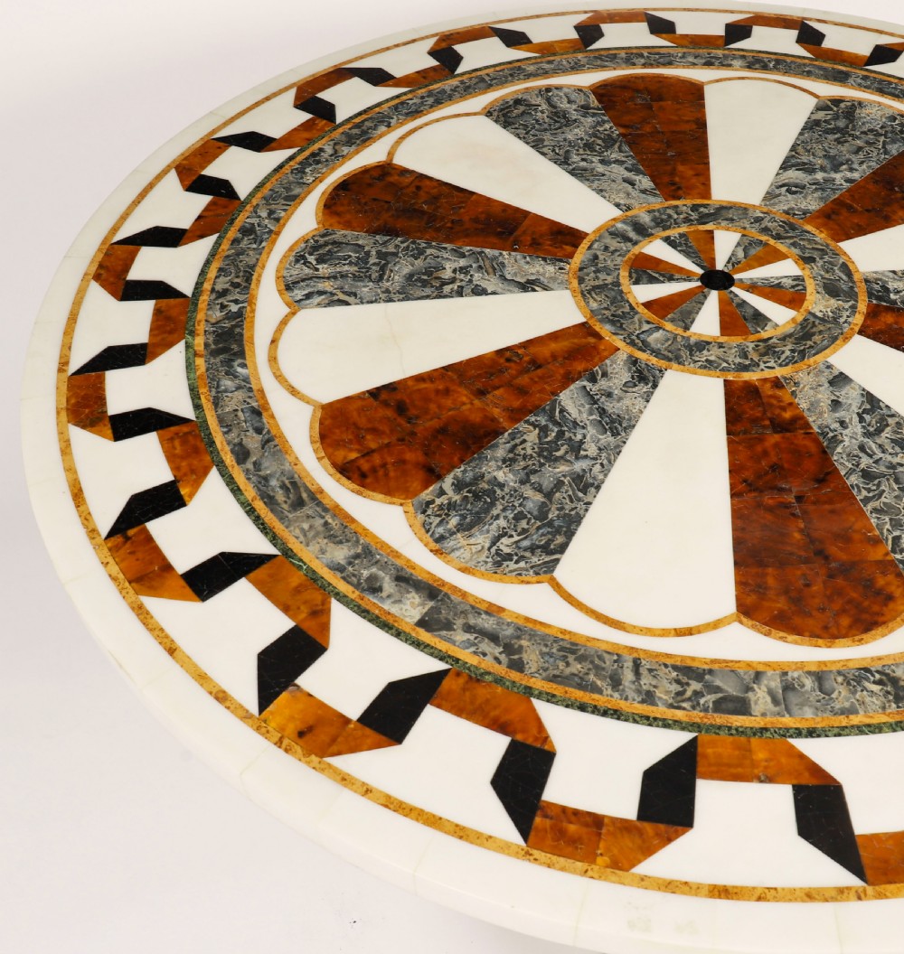 A circular centre table featuring an intricate geometric inlaid marble top supported by three carved gilt dolphin figures on a triform marble base. View V