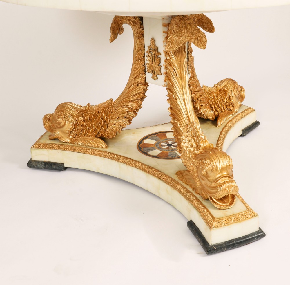 A circular centre table featuring an intricate geometric inlaid marble top supported by three carved gilt dolphin figures on a triform marble base. View IX