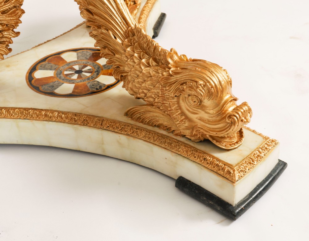 A circular centre table featuring an intricate geometric inlaid marble top supported by three carved gilt dolphin figures on a triform marble base. View X