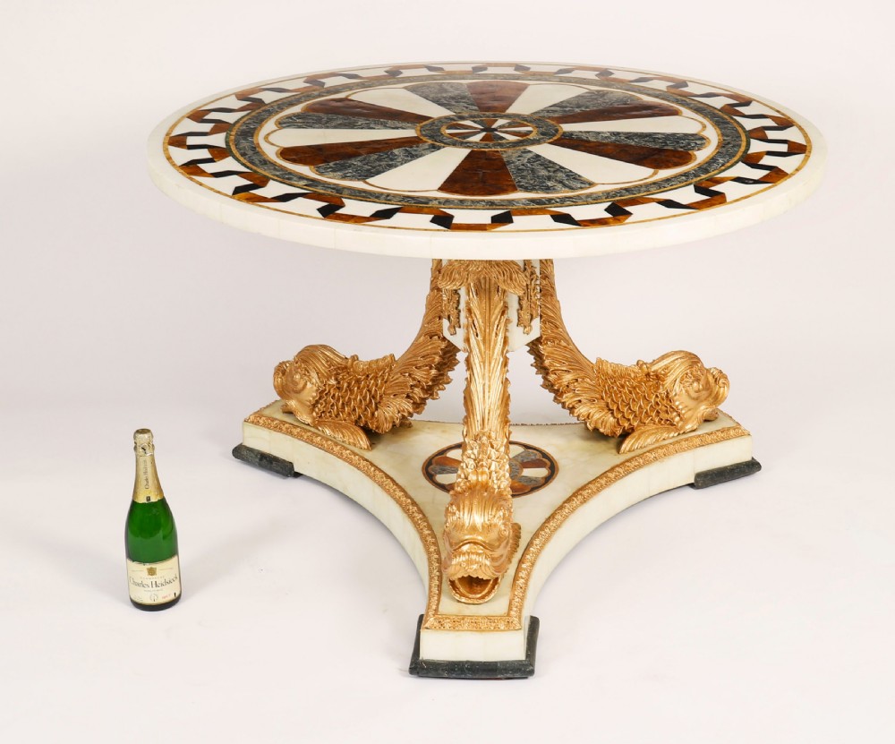 A circular centre table featuring an intricate geometric inlaid marble top supported by three carved gilt dolphin figures on a triform marble base. View XV