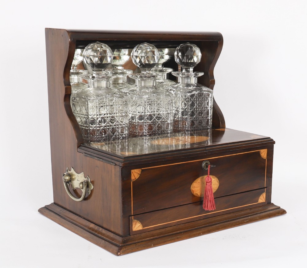 A 19th-century inlaid mahogany tantalus box containing three cut crystal decanters arranged in front of a mirrored back.