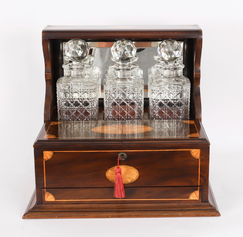A 19th-century inlaid mahogany tantalus box containing three cut crystal decanters arranged in front of a mirrored back. View II