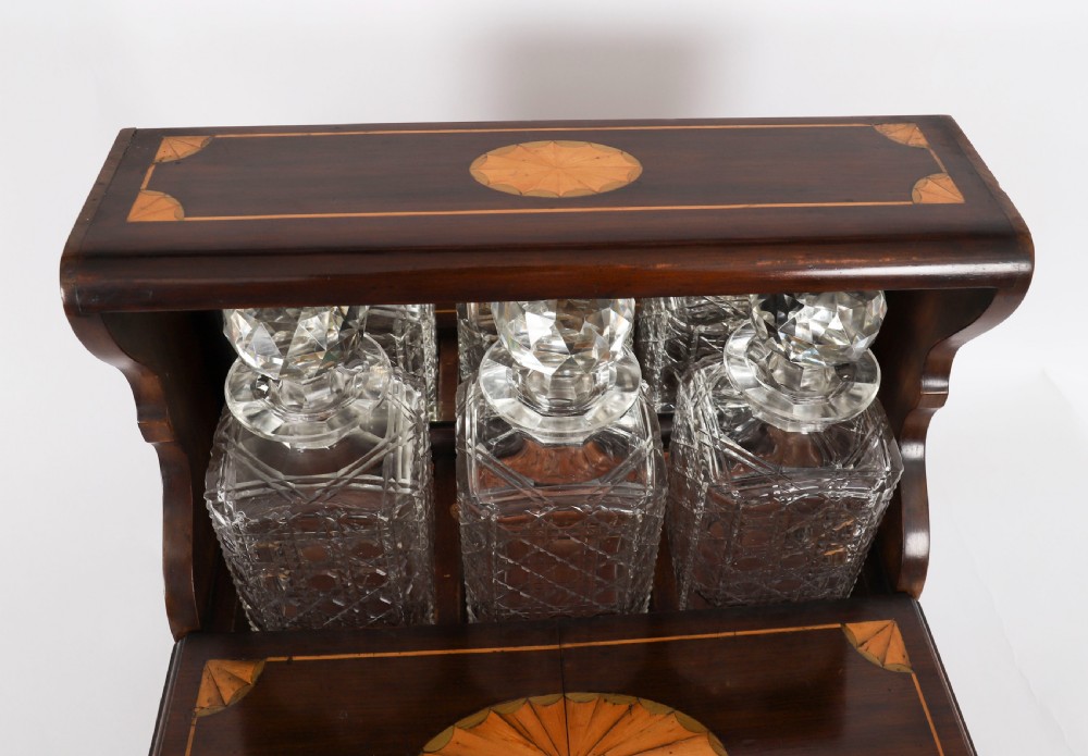 A 19th-century inlaid mahogany tantalus box containing three cut crystal decanters arranged in front of a mirrored back. View IX