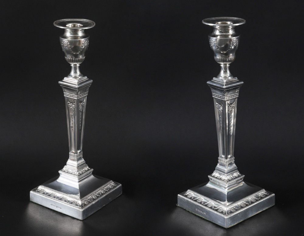 A pair of 19th-century silver-plated Neo-Classical candlesticks with tapered square shafts, urn-shaped nozzles, and festoon decoration on square bases.