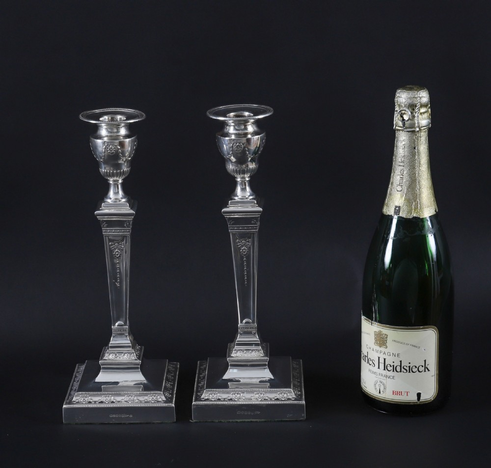 A pair of 19th-century silver-plated Neo-Classical candlesticks with tapered square shafts, urn-shaped nozzles, and festoon decoration on square bases. View XIV