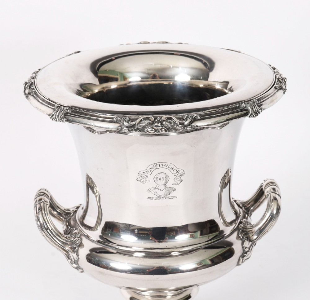 A pair of silver-plated urn-shaped wine coolers featuring scrolled side handles, engraved central crests, and circular pedestal bases. View V