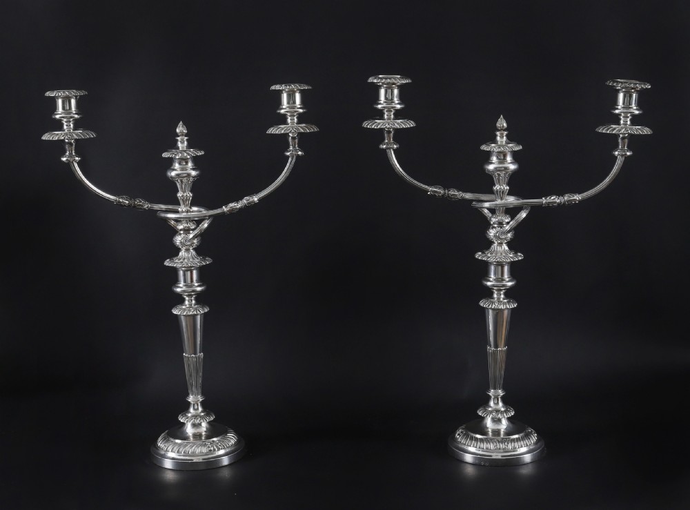 A pair of silver three-light candelabra featuring fluted columns, reeded scrolling branches, and gadrooned rims on circular bases.