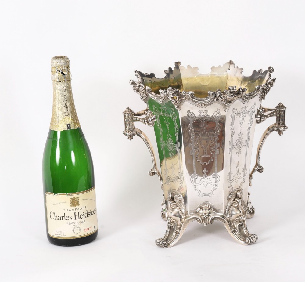 A nineteenth-century silver-plated wine cooler featuring engraved panels, cast scroll feet, side handles, and a gilded interior wash. View XV