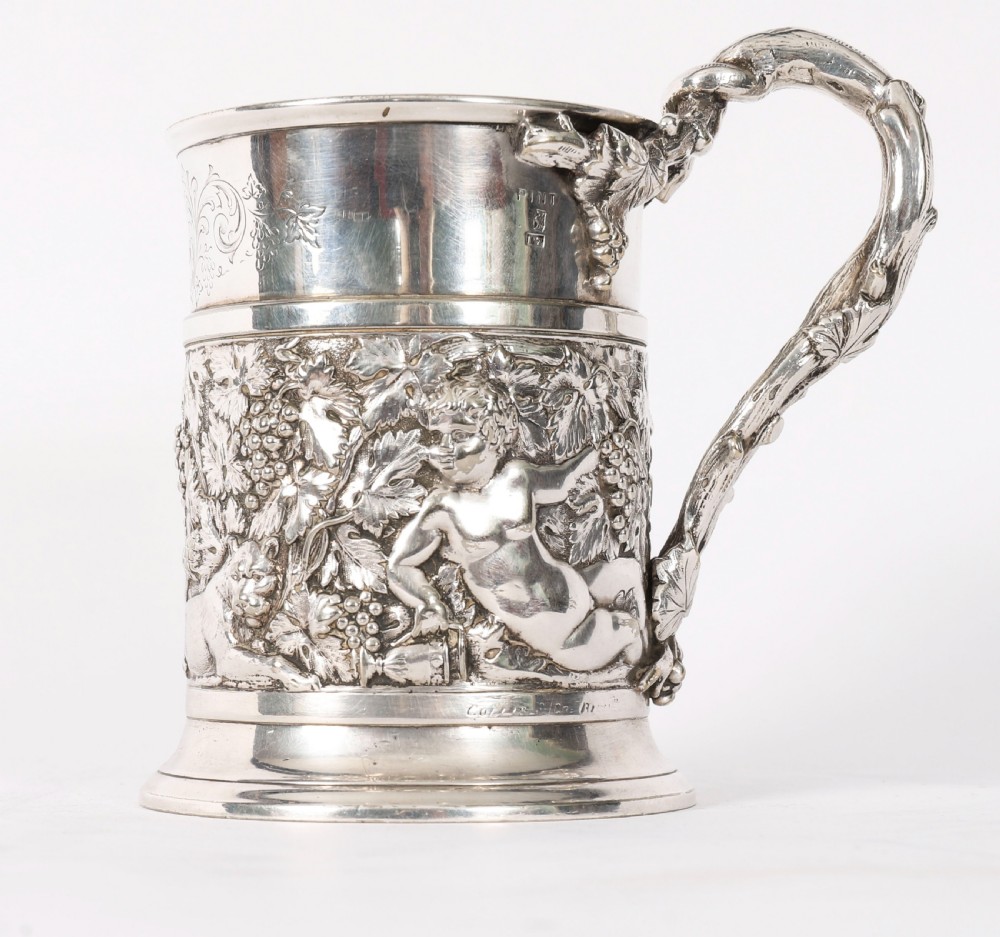 A Victorian silver-plated mug featuring embossed putti and grapevine motifs, an engraved rim, a pint capacity mark, and a naturalistic branch-shaped handle. View IV