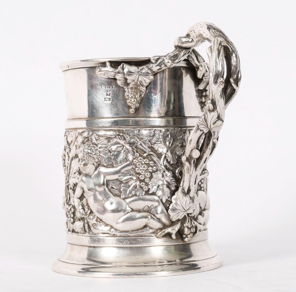 A Victorian silver-plated mug featuring embossed putti and grapevine motifs, an engraved rim, a pint capacity mark, and a naturalistic branch-shaped handle. View VII