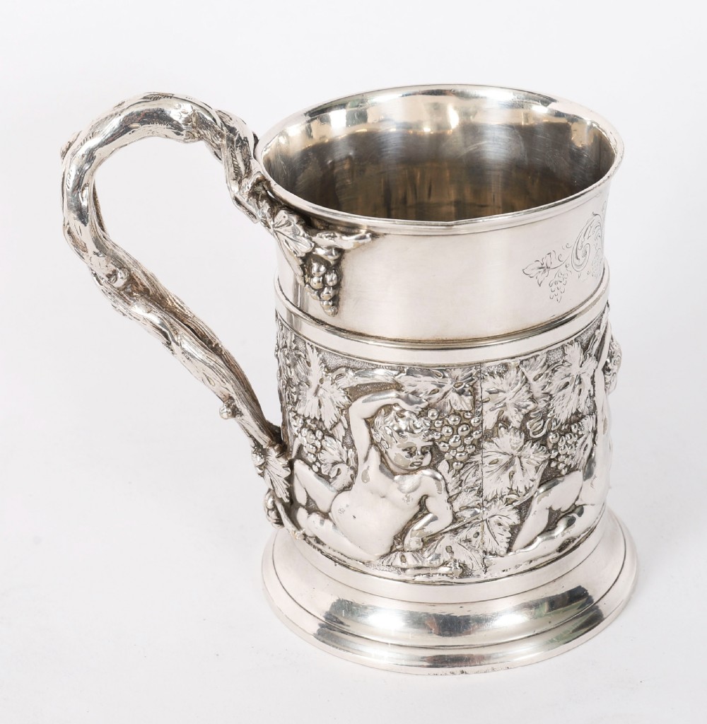 A Victorian silver-plated mug featuring embossed putti and grapevine motifs, an engraved rim, a pint capacity mark, and a naturalistic branch-shaped handle. View X