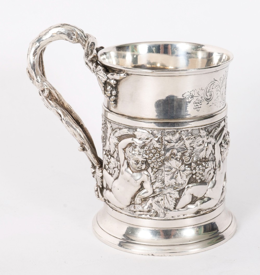 A Victorian silver-plated mug featuring embossed putti and grapevine motifs, an engraved rim, a pint capacity mark, and a naturalistic branch-shaped handle. View XIV