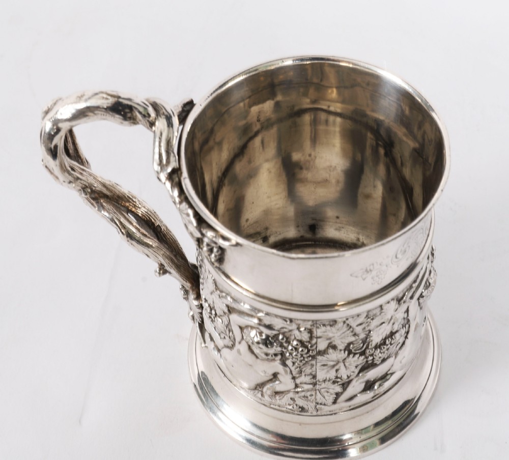 A Victorian silver-plated mug featuring embossed putti and grapevine motifs, an engraved rim, a pint capacity mark, and a naturalistic branch-shaped handle. View XVII