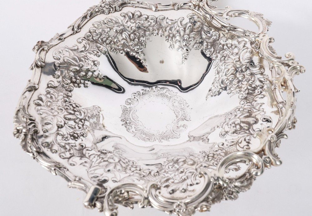 An ornate mid-19th-century Victorian silver-plated fruit basket with a high scroll swing handle, chased leaf patterns, scalloped rim, and pedestal base. View II