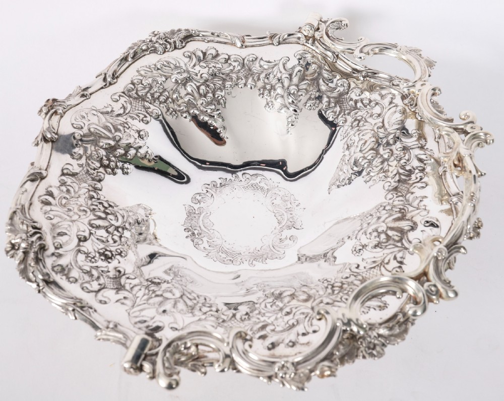 An ornate mid-19th-century Victorian silver-plated fruit basket with a high scroll swing handle, chased leaf patterns, scalloped rim, and pedestal base. View IV