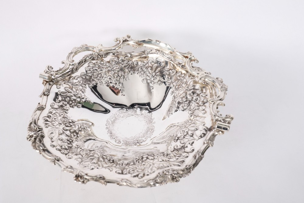 An ornate mid-19th-century Victorian silver-plated fruit basket with a high scroll swing handle, chased leaf patterns, scalloped rim, and pedestal base. View V