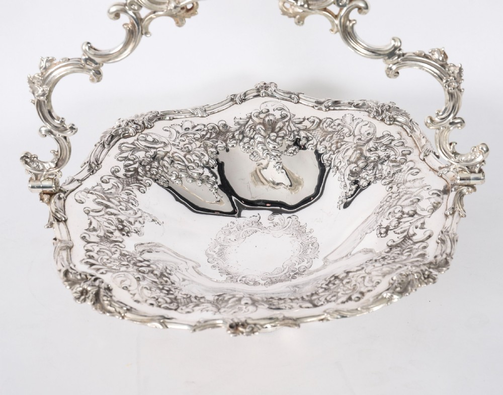 An ornate mid-19th-century Victorian silver-plated fruit basket with a high scroll swing handle, chased leaf patterns, scalloped rim, and pedestal base. View VII