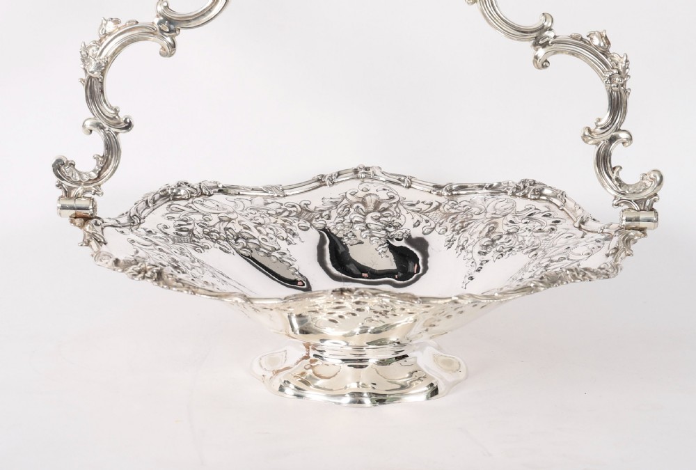 An ornate mid-19th-century Victorian silver-plated fruit basket with a high scroll swing handle, chased leaf patterns, scalloped rim, and pedestal base. View XI