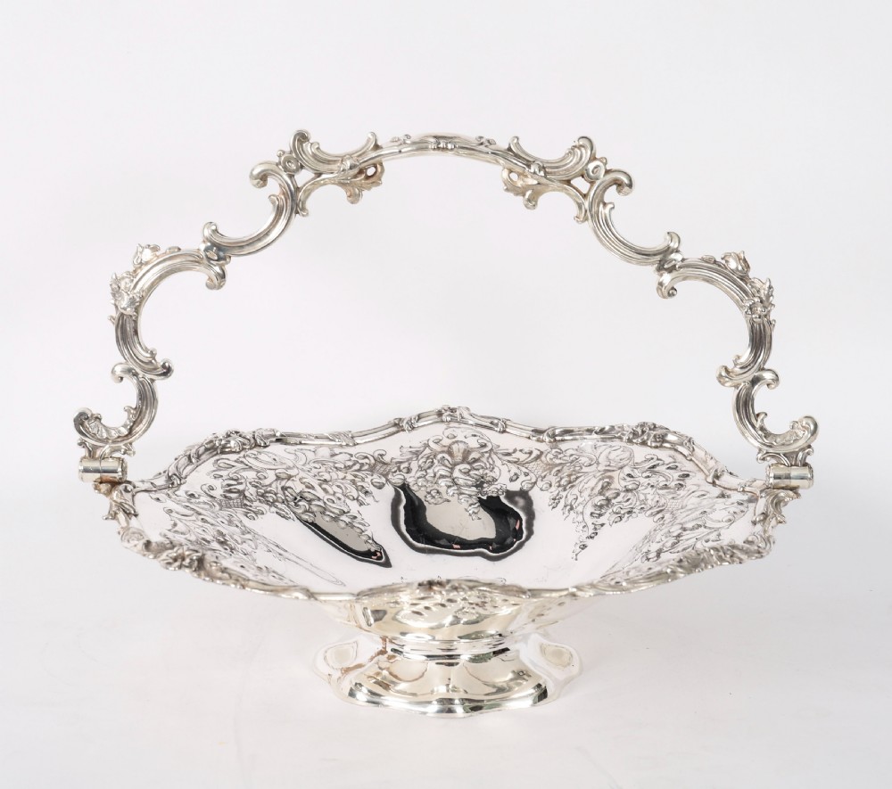 An ornate mid-19th-century Victorian silver-plated fruit basket with a high scroll swing handle, chased leaf patterns, scalloped rim, and pedestal base. View XII