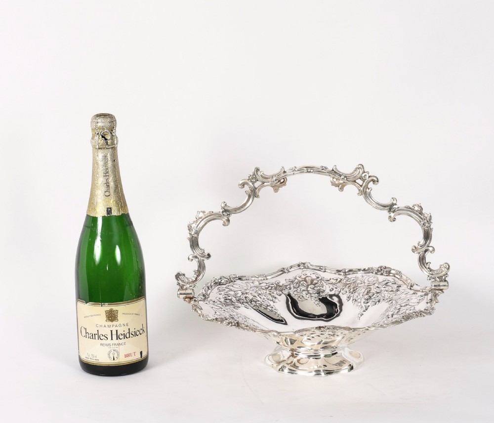 An ornate mid-19th-century Victorian silver-plated fruit basket with a high scroll swing handle, chased leaf patterns, scalloped rim, and pedestal base. View XIII