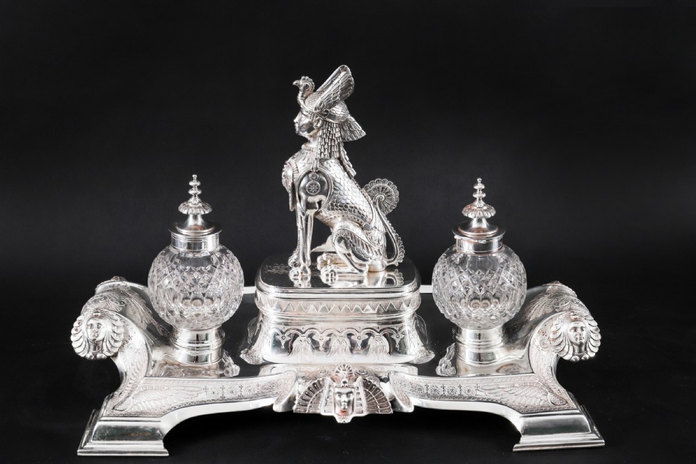 A Victorian silver-plated inkstand featuring a central winged sphinx sculpture flanked by two cut glass inkwell bottles.