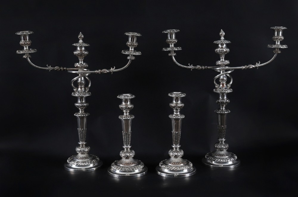 A four-piece set of 18th-century George III Old Sheffield silver-plated candelabra and matching candlesticks with fluted stems and leaf motifs.