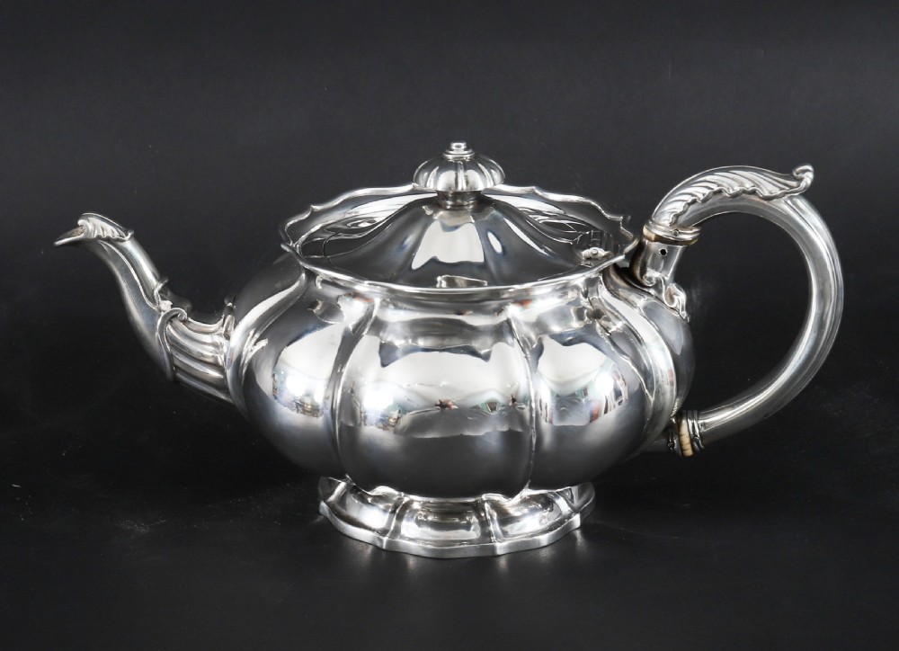 A Georgian sterling silver teapot featuring a lobed melon-shaped body, leaf-engraved spout, and insulated handle. View IV