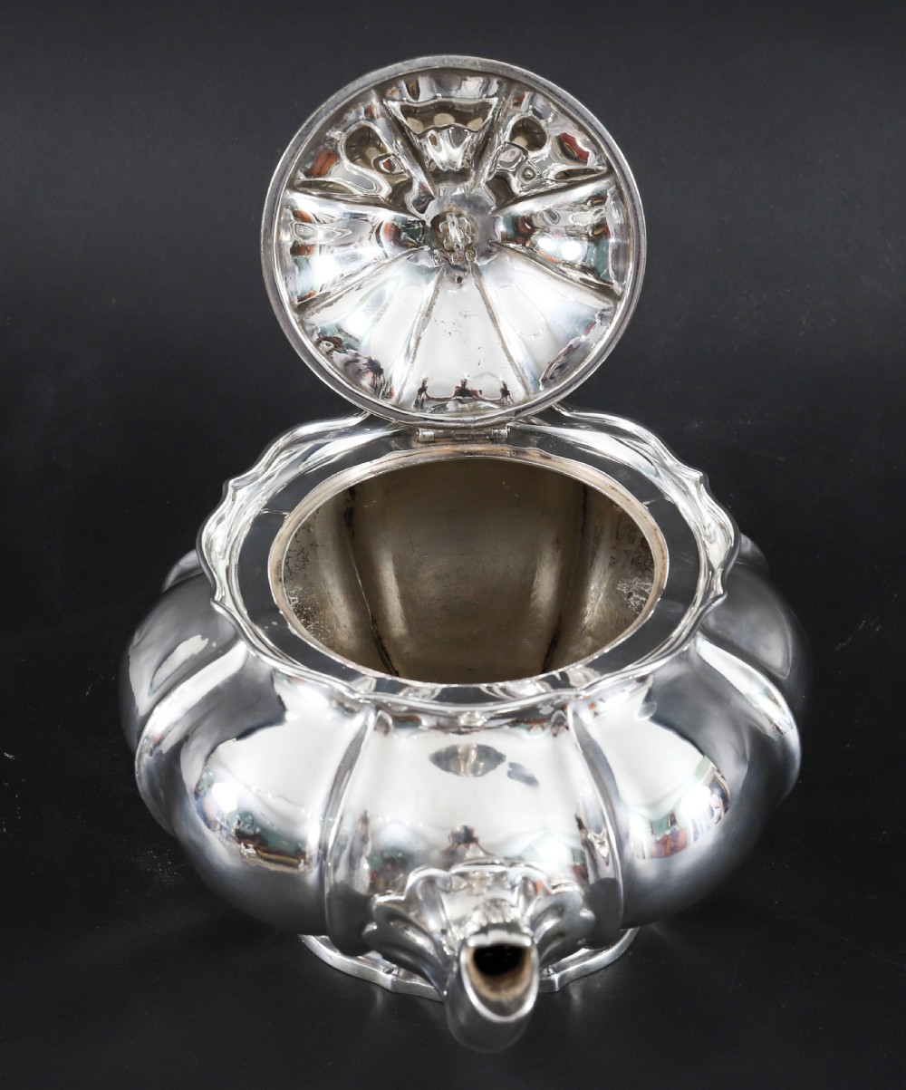 A Georgian sterling silver teapot featuring a lobed melon-shaped body, leaf-engraved spout, and insulated handle. View XI