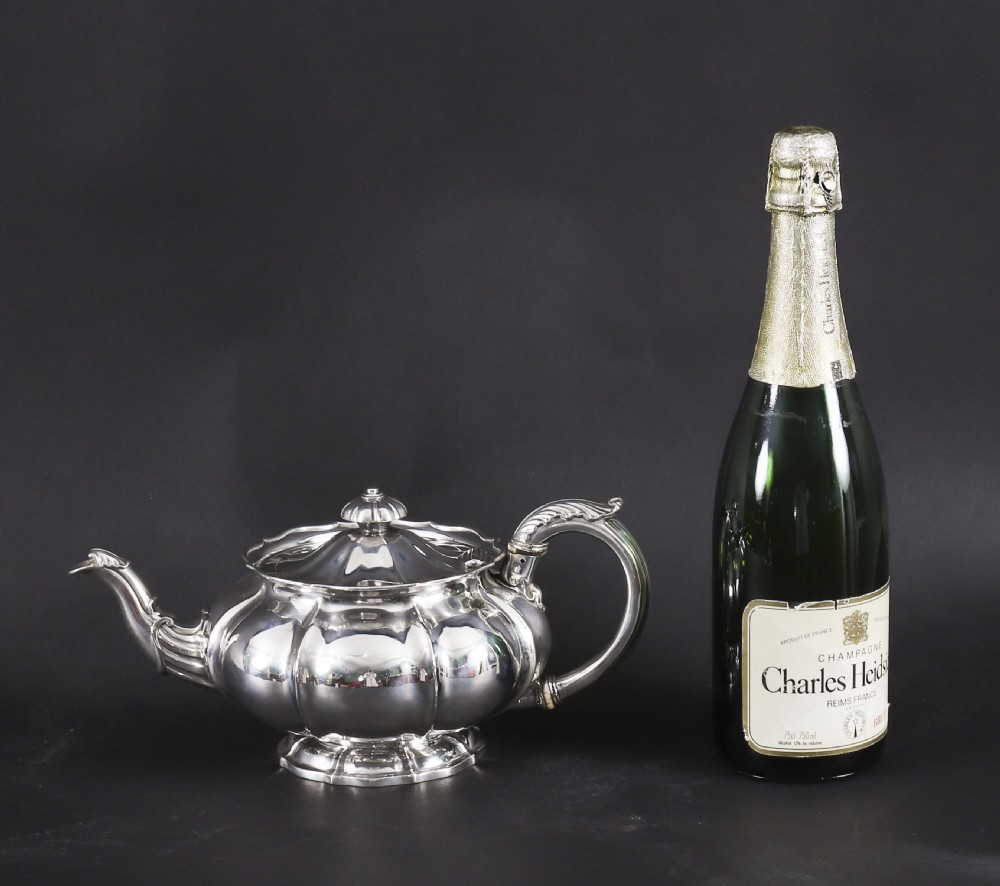 A Georgian sterling silver teapot featuring a lobed melon-shaped body, leaf-engraved spout, and insulated handle. View XVI