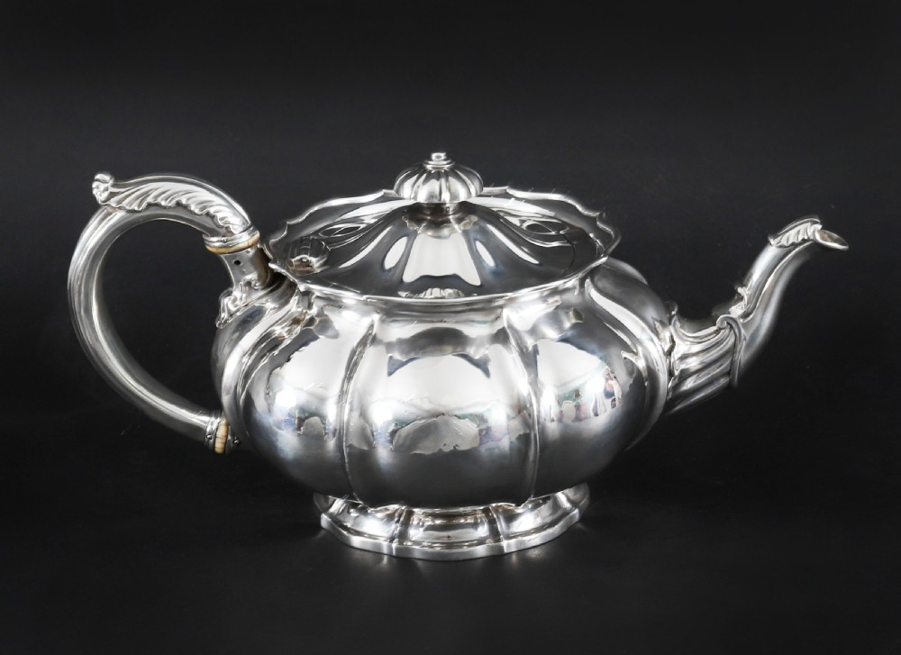 A Georgian sterling silver teapot featuring a lobed melon-shaped body, leaf-engraved spout, and insulated handle. View XVII