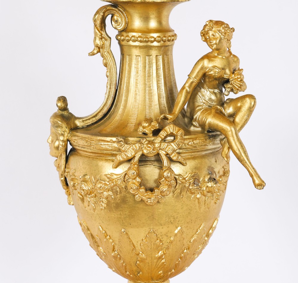 A pair of Neoclassical ormolu urn-form table lamps featuring classical figures mounted on square pink marble bases with cream pleated shades. View IX
