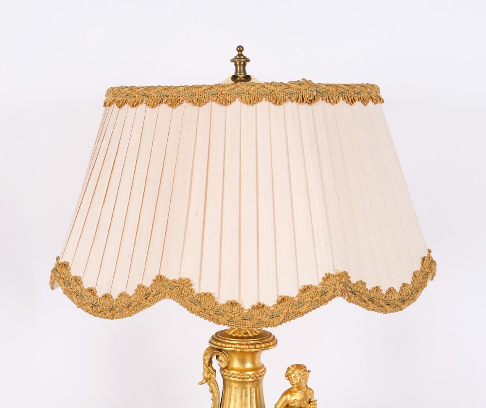 A pair of Neoclassical ormolu urn-form table lamps featuring classical figures mounted on square pink marble bases with cream pleated shades. View X