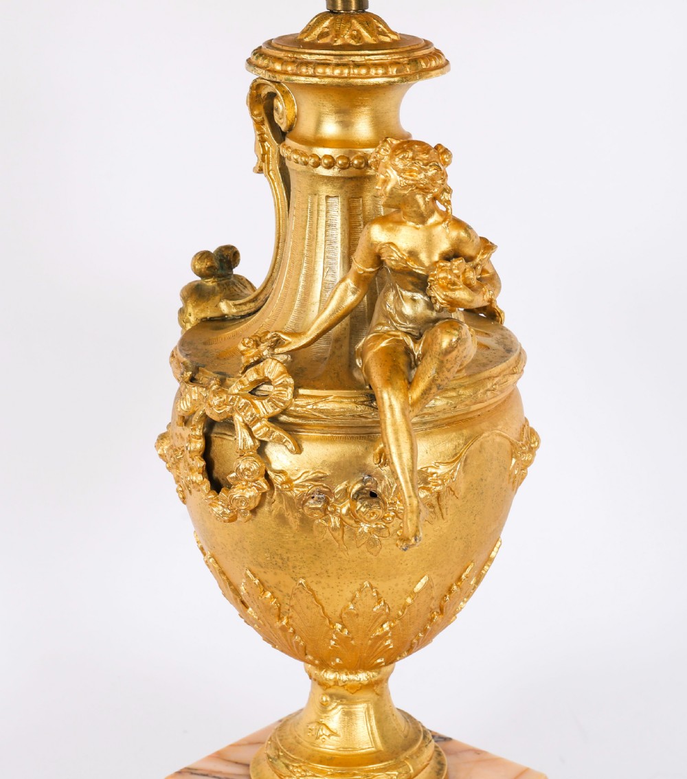 A pair of Neoclassical ormolu urn-form table lamps featuring classical figures mounted on square pink marble bases with cream pleated shades. View XV