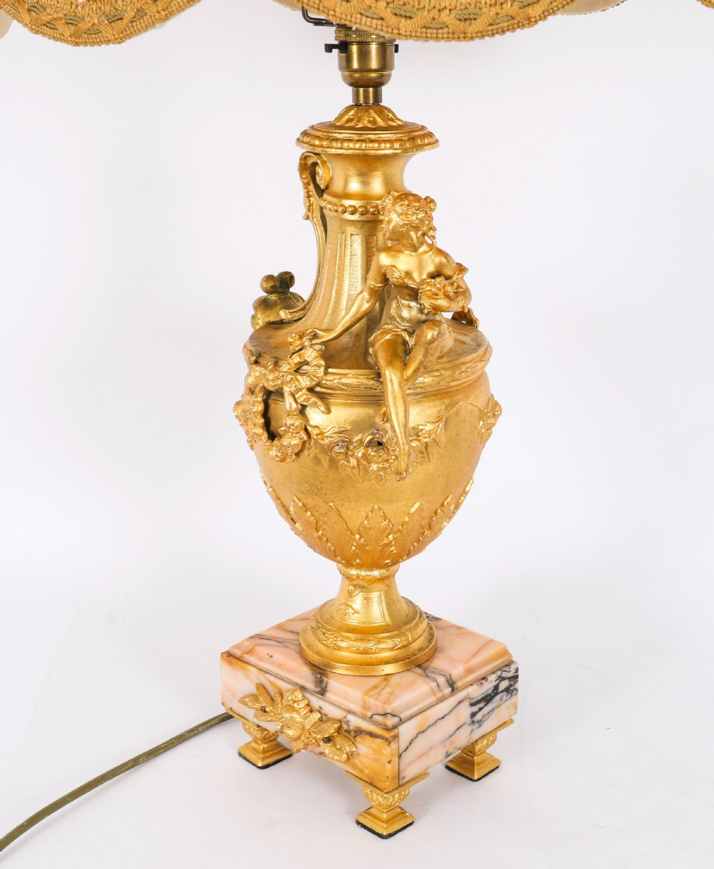 A pair of Neoclassical ormolu urn-form table lamps featuring classical figures mounted on square pink marble bases with cream pleated shades. View XVI