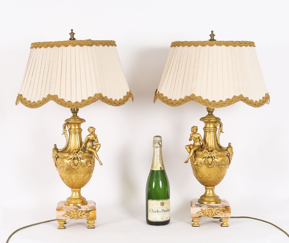 A pair of Neoclassical ormolu urn-form table lamps featuring classical figures mounted on square pink marble bases with cream pleated shades. View XIX