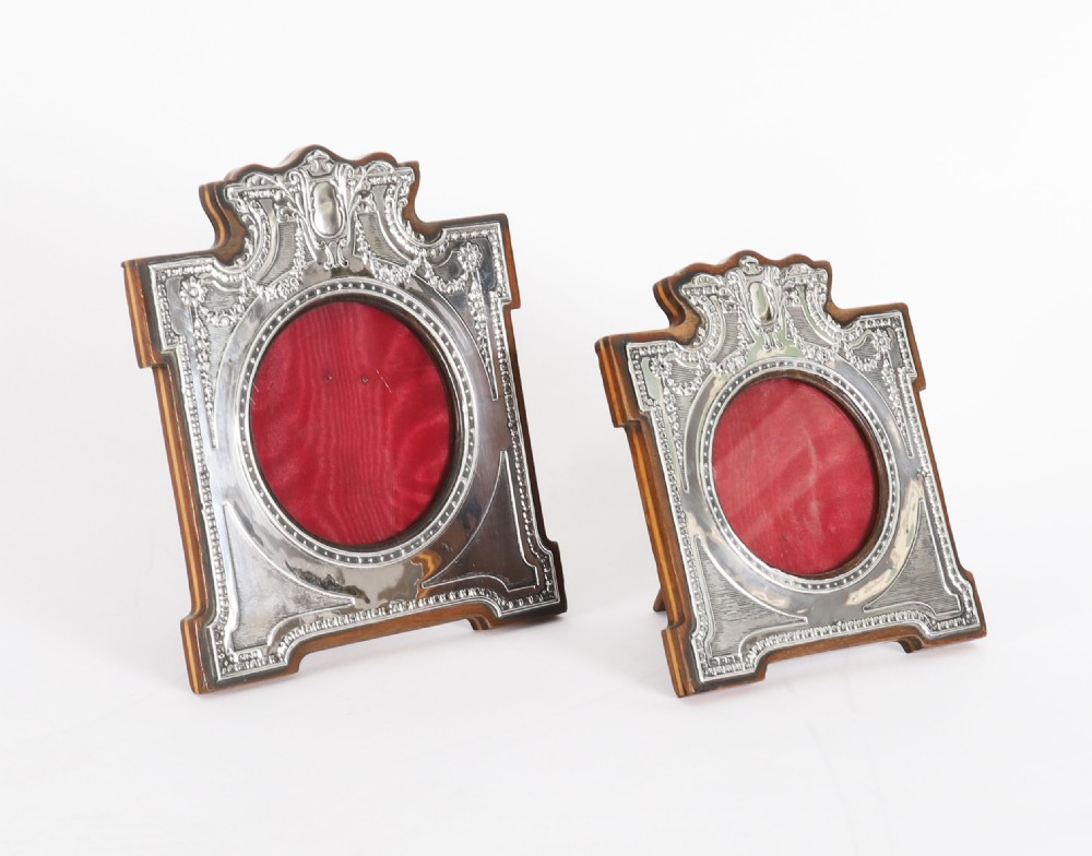 A pair of Edwardian sterling silver photo frames with wooden easel backs and oval apertures lined in red fabric.