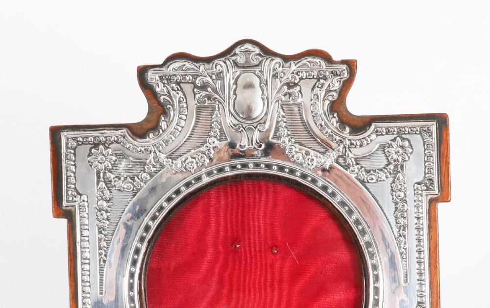 A pair of Edwardian sterling silver photo frames with wooden easel backs and oval apertures lined in red fabric. View VI