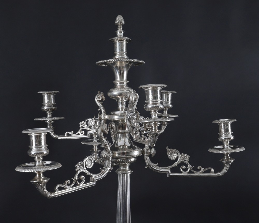 An ornate Victorian silver-plated multi-arm table centrepiece candelabra featuring scrollwork branches, a fluted column stem, and a pediment base adorned with mythical creatures. View IV