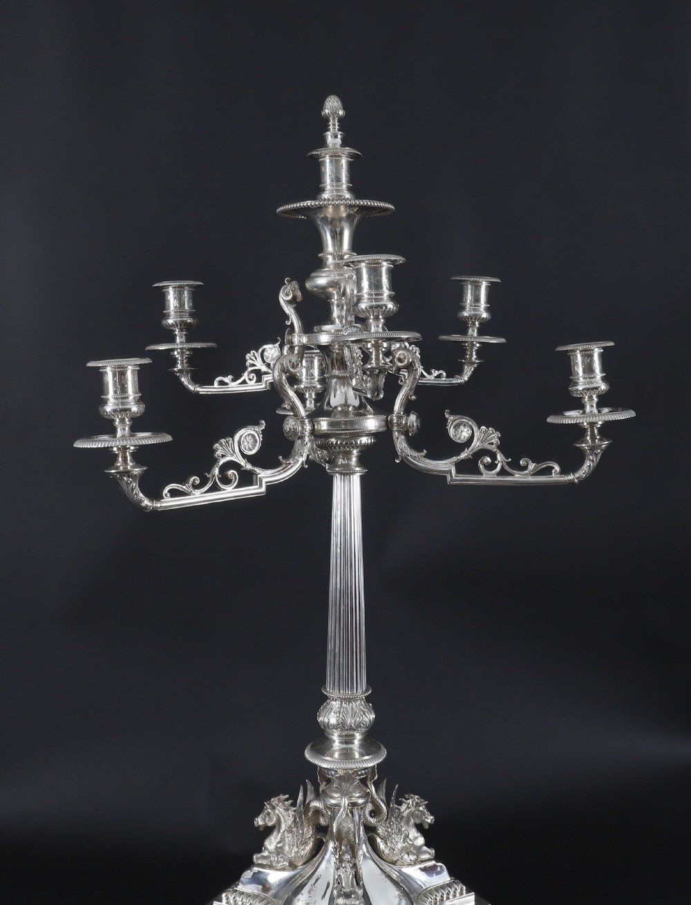 An ornate Victorian silver-plated multi-arm table centrepiece candelabra featuring scrollwork branches, a fluted column stem, and a pediment base adorned with mythical creatures. View VII