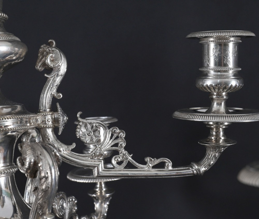 An ornate Victorian silver-plated multi-arm table centrepiece candelabra featuring scrollwork branches, a fluted column stem, and a pediment base adorned with mythical creatures. View VIII