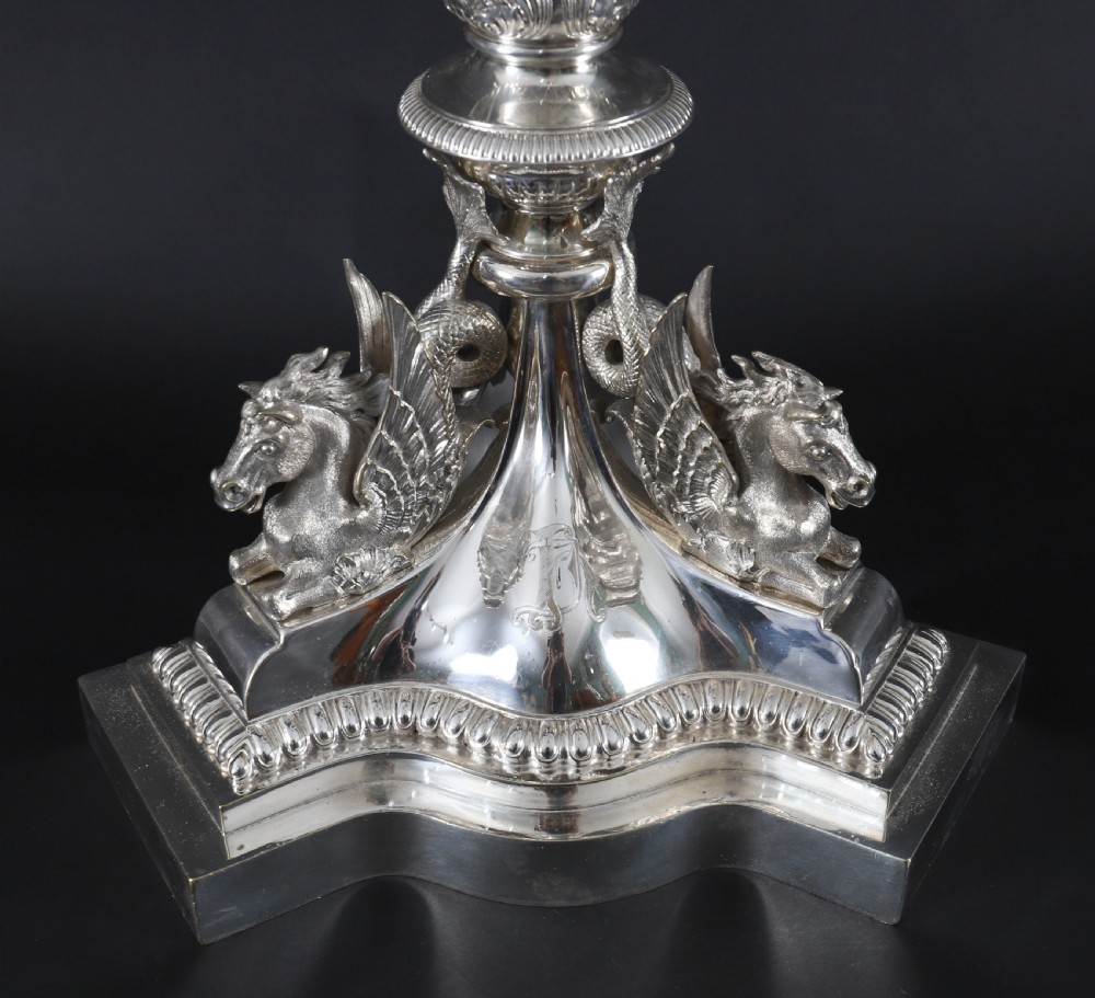 An ornate Victorian silver-plated multi-arm table centrepiece candelabra featuring scrollwork branches, a fluted column stem, and a pediment base adorned with mythical creatures. View XV