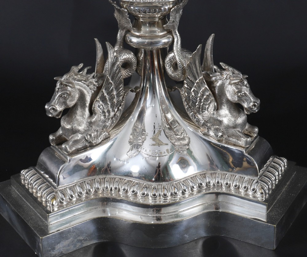 An ornate Victorian silver-plated multi-arm table centrepiece candelabra featuring scrollwork branches, a fluted column stem, and a pediment base adorned with mythical creatures. View XVIII