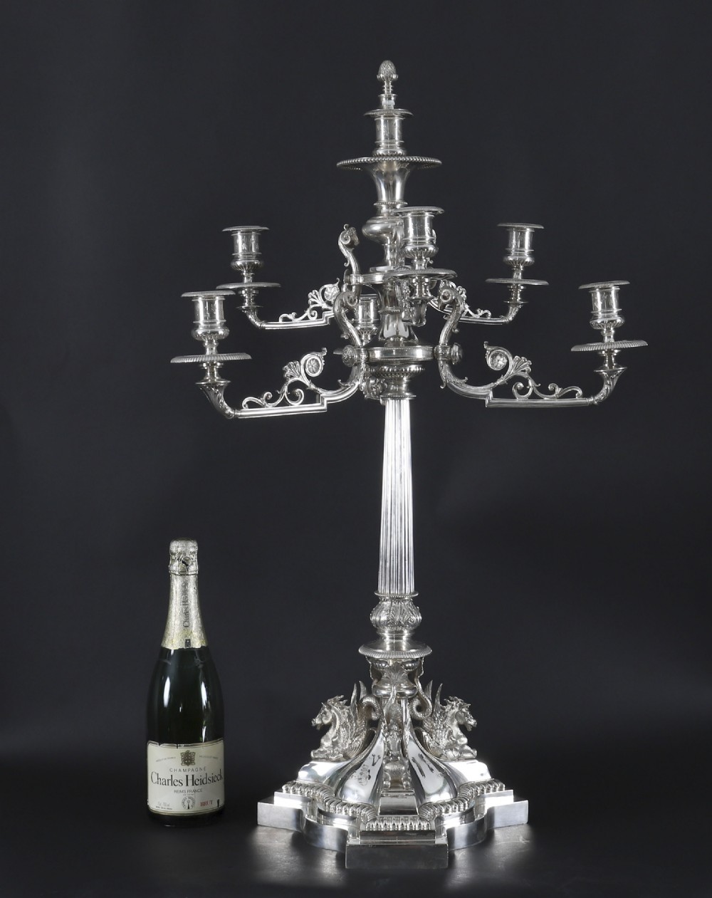 An ornate Victorian silver-plated multi-arm table centrepiece candelabra featuring scrollwork branches, a fluted column stem, and a pediment base adorned with mythical creatures. View XIX