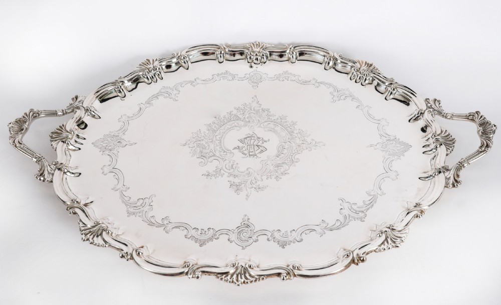 An oval Victorian silver plated serving tray featuring engraved scrollwork, cast shell borders, and dual side handles.
