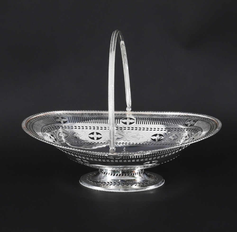 An antique silver-plated oval fruit basket featuring delicate pierced metalwork, engraved geometric motifs, a beaded pedestal foot, and a tall arched handle. View II