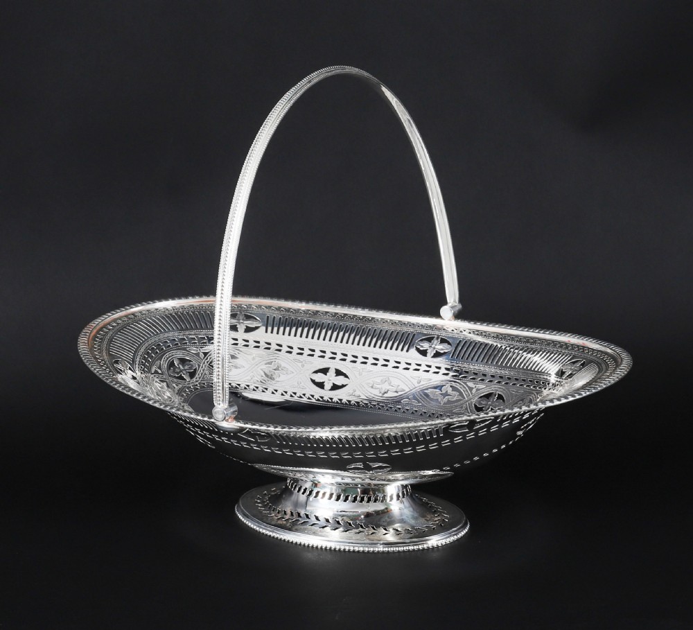 An antique silver-plated oval fruit basket featuring delicate pierced metalwork, engraved geometric motifs, a beaded pedestal foot, and a tall arched handle. View III