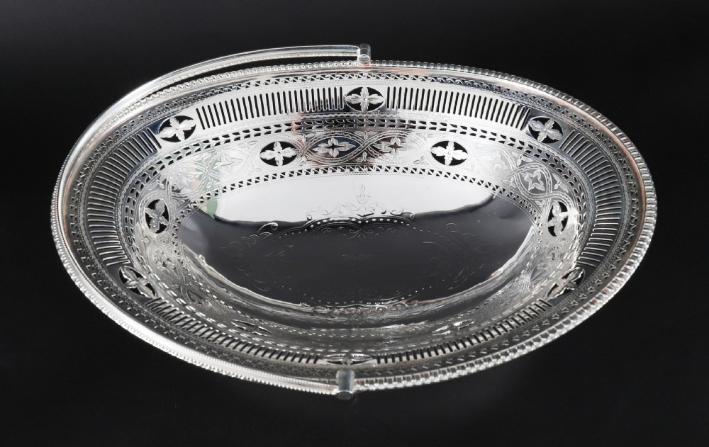 An antique silver-plated oval fruit basket featuring delicate pierced metalwork, engraved geometric motifs, a beaded pedestal foot, and a tall arched handle. View IV