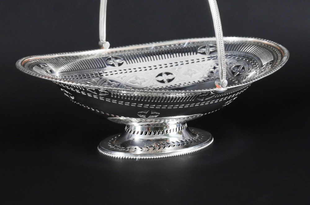 An antique silver-plated oval fruit basket featuring delicate pierced metalwork, engraved geometric motifs, a beaded pedestal foot, and a tall arched handle. View VII