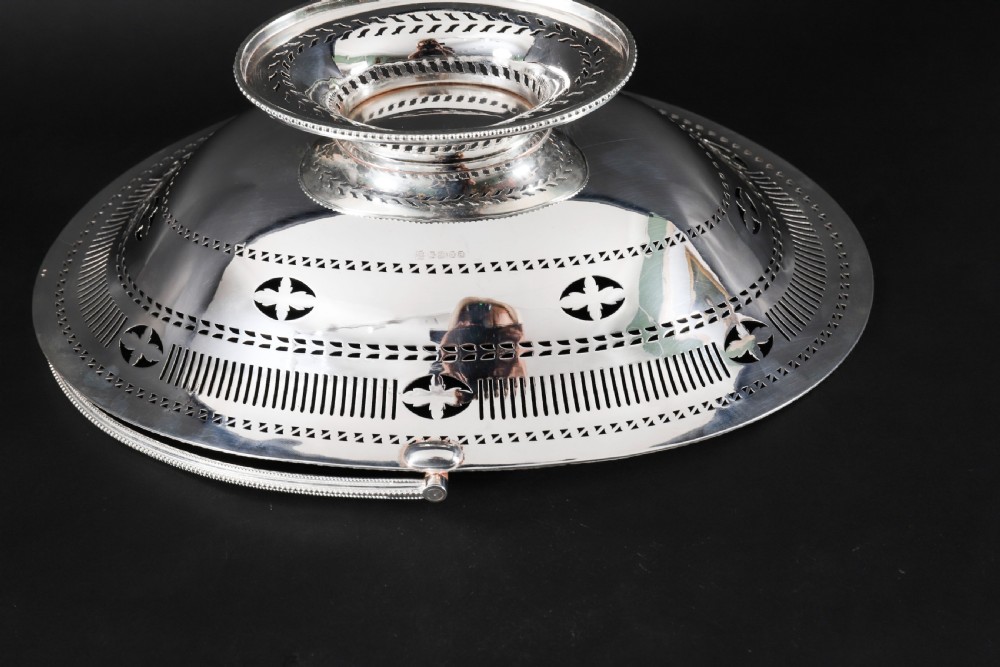 An antique silver-plated oval fruit basket featuring delicate pierced metalwork, engraved geometric motifs, a beaded pedestal foot, and a tall arched handle. View X