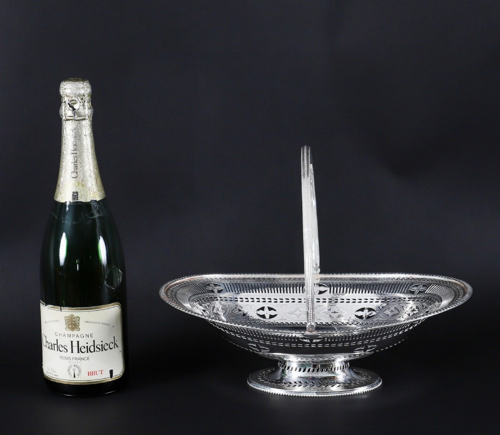 An antique silver-plated oval fruit basket featuring delicate pierced metalwork, engraved geometric motifs, a beaded pedestal foot, and a tall arched handle. View XV